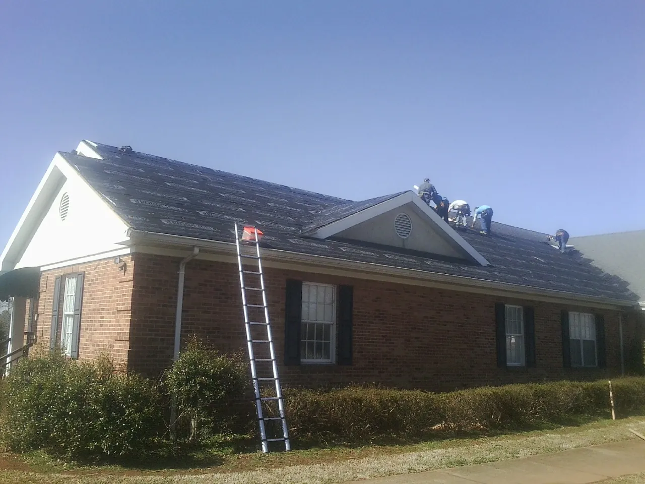 Crew tearing shingles off a brick ranch roof with a ladder set — Emergency Roof Repair work by our crew in Hacker Valley