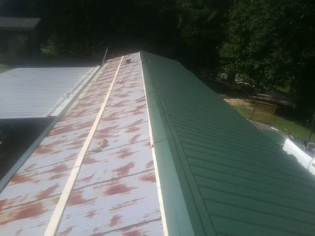 Old rusted panels beside newly installed green metal roofing — Wind Damage Roof Repair by Roofing Brothers in Hacker Valley