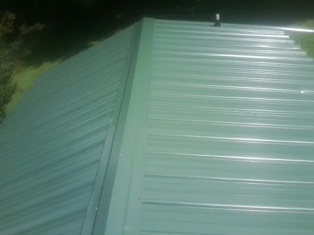 New green metal panels meeting at the ridge of a roof — Flat Roof Repair work by our crew in Hacker Valley