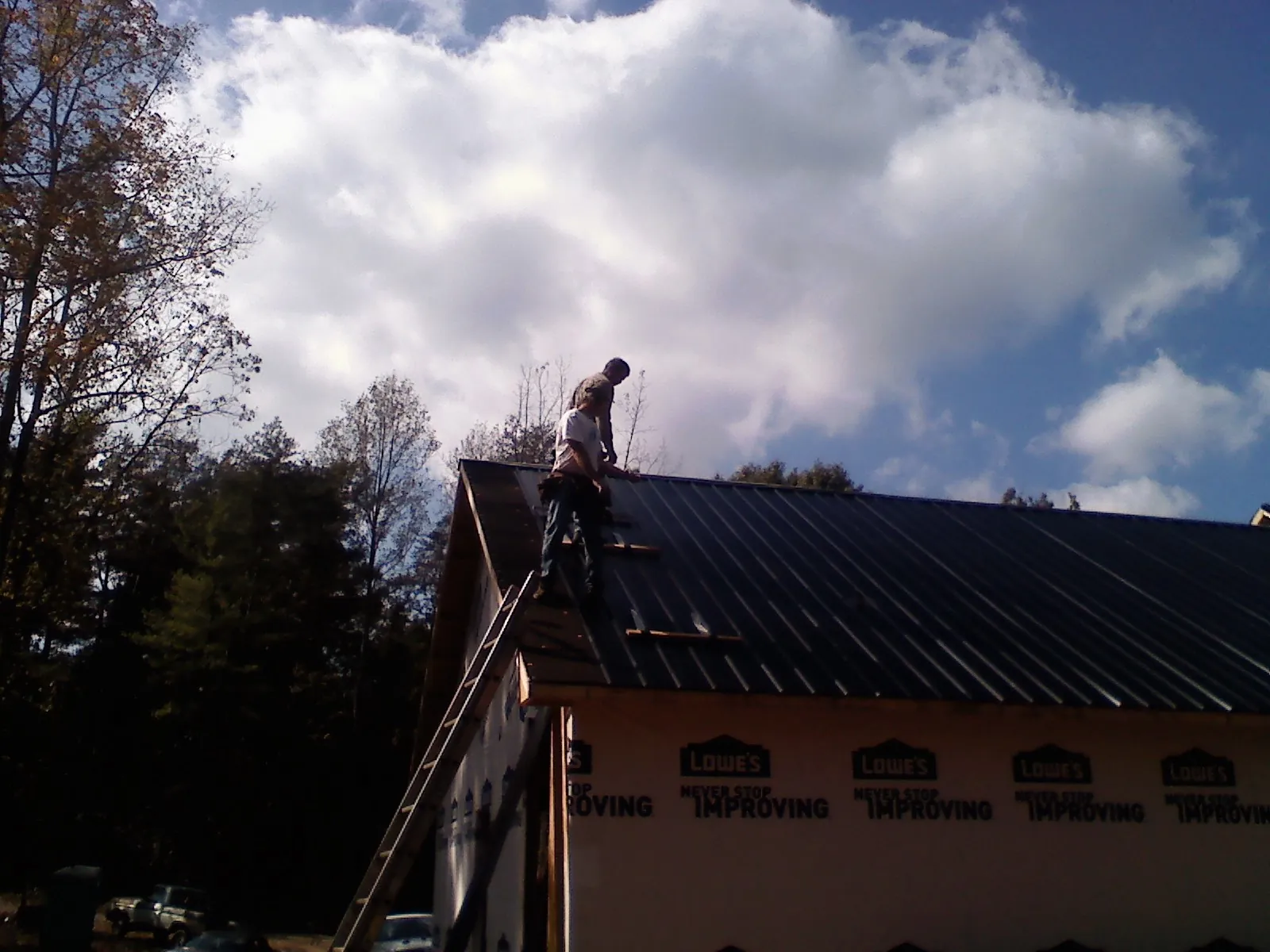 Roofer fastening dark metal panels high against a cloudy sky, from a Roof Inspection job in Hacker Valley