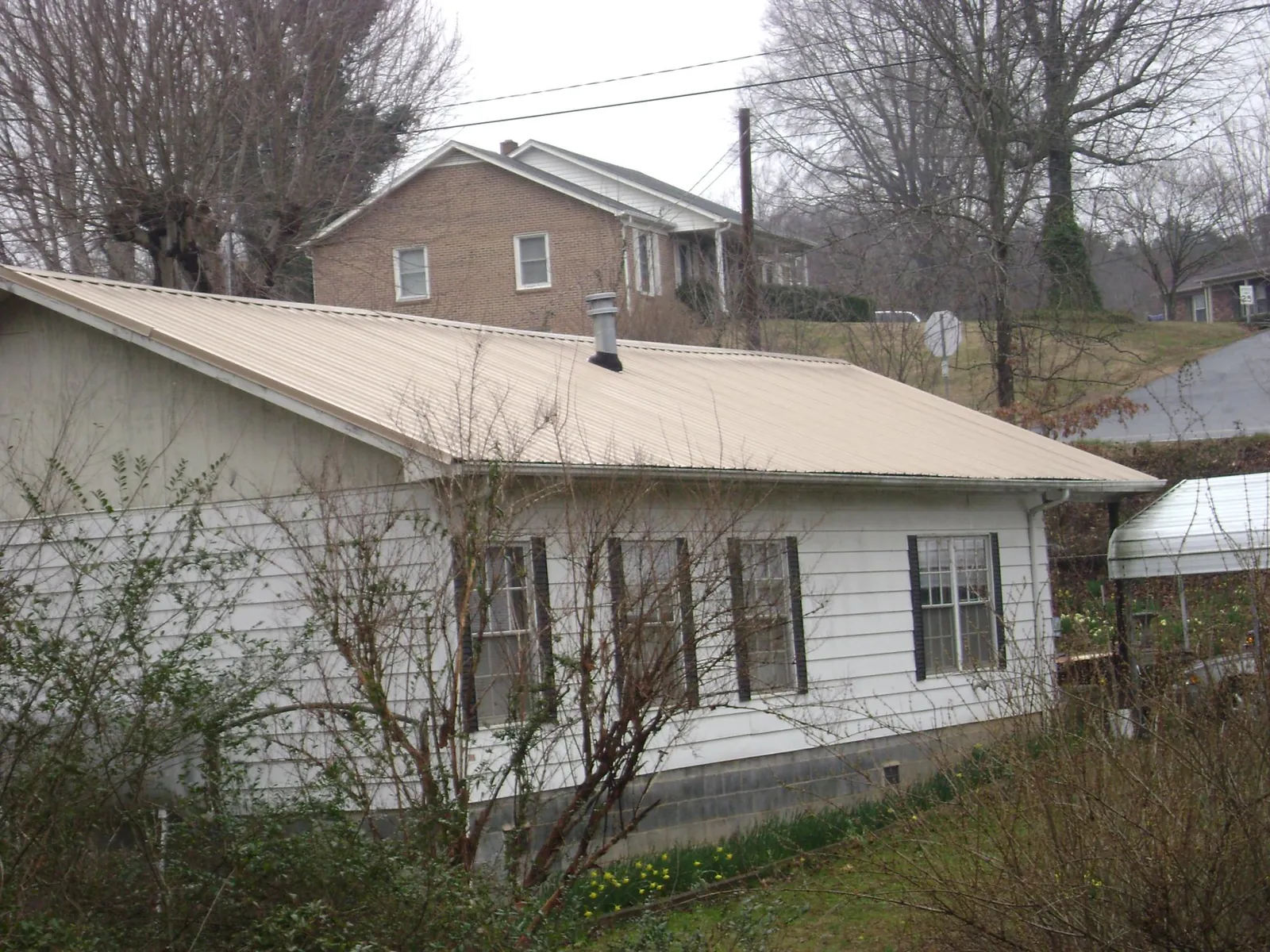 Tan metal roof on a white sided house set into a hillside — Commercial Roofing by Roofing Brothers in Hacker Valley